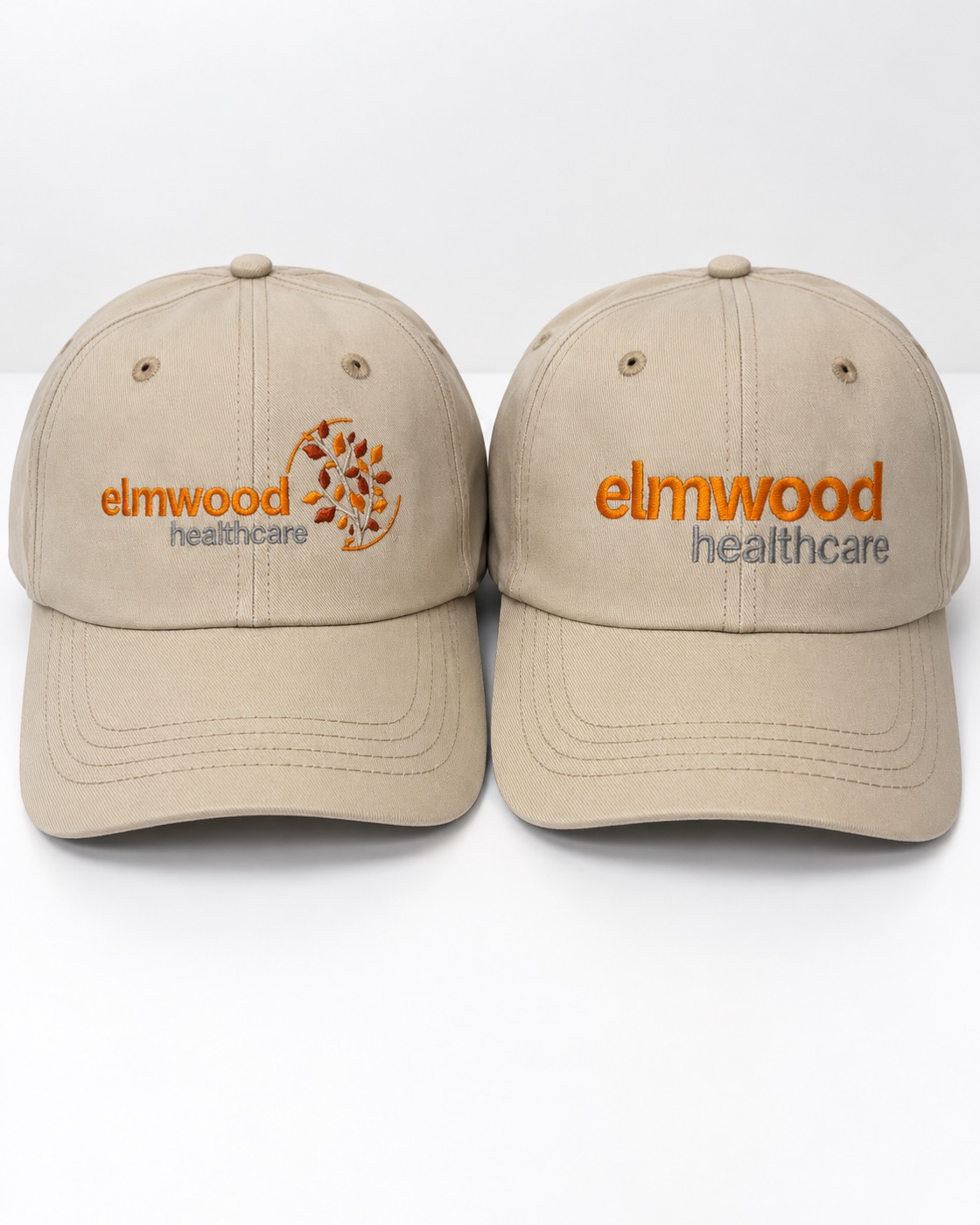 Two stone-colored caps embroidered with the Elmwood Healthcare logo in orange and gray — one with the leaf mark, one lettering only.