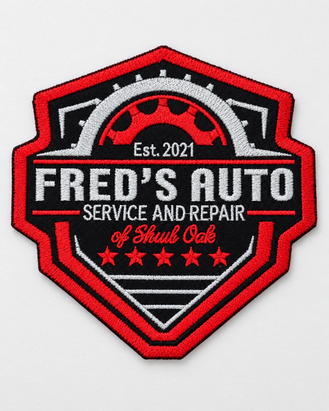 Embroidered shield patch with a red merrowed border reading Fred’s Auto, Service and Repair of Shrub Oak, Est. 2021, stitched in red, white and gray on black with a gear and five stars.